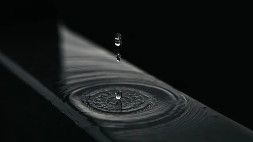 Water droplets falling onto a still surface and forming ripples against a dark background