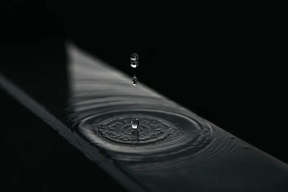 Close-up of water drops splashing into a thin layer of water, sending out circular ripples