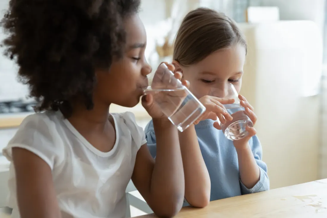 Two girls drinking glasses of water at a wooden kitchen table