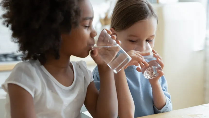 Two girls drinking glasses of water at a wooden kitchen table