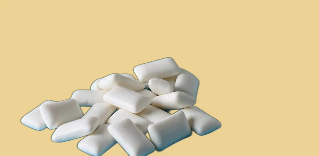 Pile of white chewing gum pellets on a pale yellow background