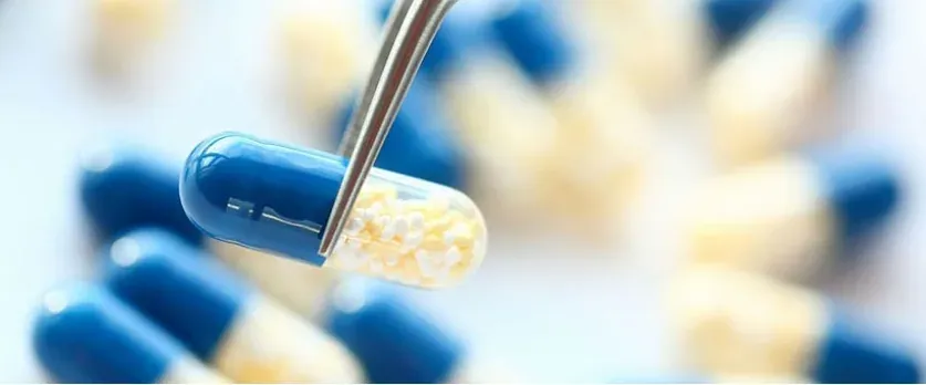 Tweezers holding a blue and clear capsule filled with small white pellets