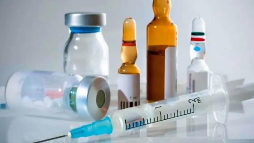 Glass vials, ampoules and a syringe with a blue-hubbed needle on a white surface
