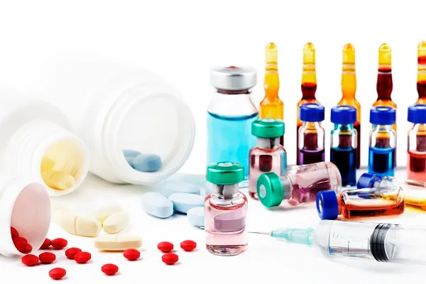 Tablets, capsules, glass vials, ampoules and a syringe spread across a white surface