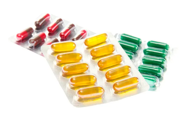 Blister packs of red and brown capsules, yellow softgels and green capsules on a white background