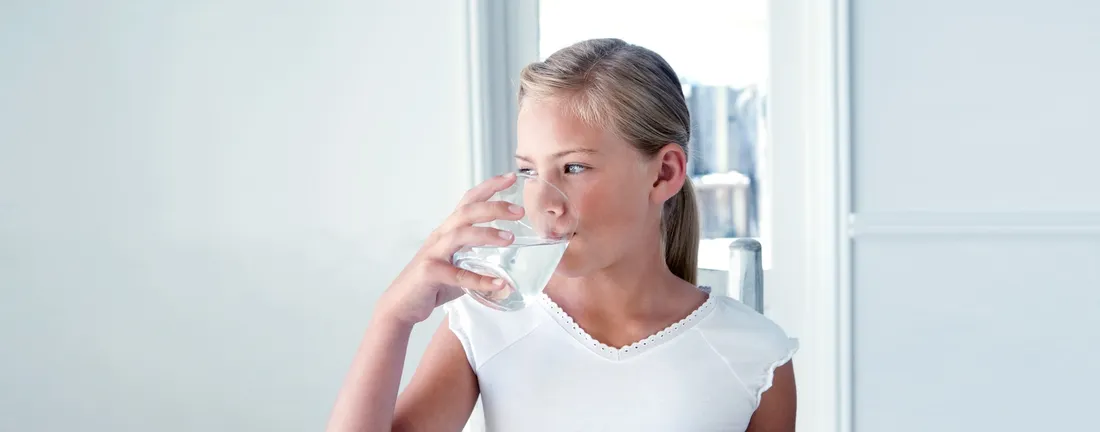 Girl drinking from a glass of water beside a bright window