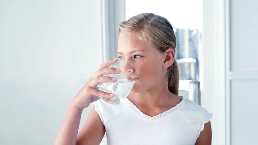 Girl drinking from a glass of water beside a bright window