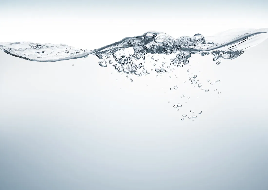 Surface of clear water with air bubbles against a pale grey background