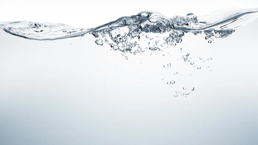 Surface of clear water with air bubbles against a pale grey background